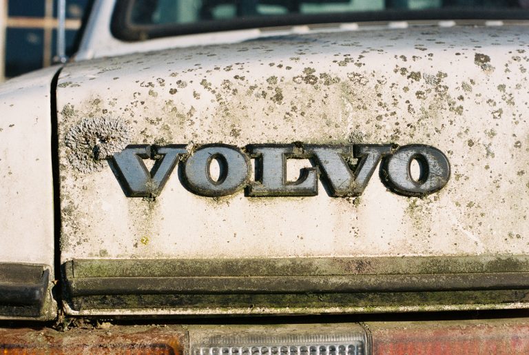 Close-up of the rear of a dirty, weathered Volvo car, with the VOLVO badge partially covered in grime and moss. Captured in a film photography style, the image highlights the vehicle’s age and neglect with an authentic, vintage feel. | Photo by Millworks Film Photography & Prints