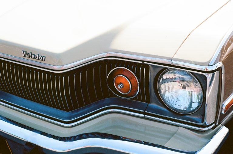 Close-up of the front end of a cream-colored classic car, captured with professional photography, showing the Matador badge, chrome trim, black grille, and a round headlight on the right side. | Photo by Millworks Film Photography & Prints