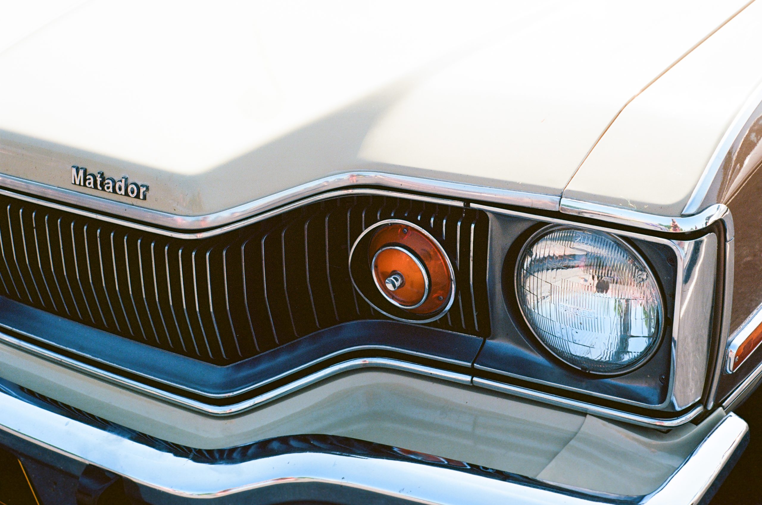 Close-up of the front end of a cream-colored classic car, captured with professional photography, showing the Matador badge, chrome trim, black grille, and a round headlight on the right side. | Photo by Millworks Film Photography & Prints