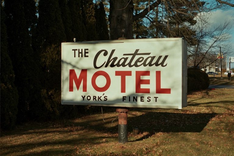A vintage sign reads The Chateau Motel Yorks Finest in bold red and black letters, standing on a grassy area with trees and a street visible in the background, captured with classic film photography for a nostalgic feel. | Photo by Millworks Film Photography & Prints