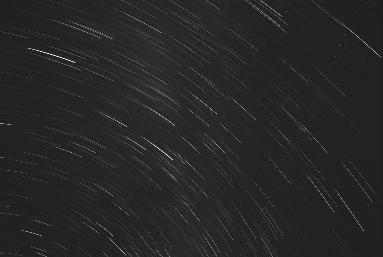 Long-exposure film photography of the night sky shows curved, white star trails against a dark background, capturing the Earths rotation in a stunning professional photo. | Photo by Millworks Film Photography & Prints