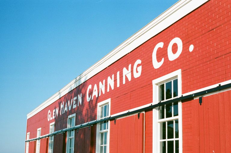 A red brick building with white trim and large white letters reading GLEN HAVEN CANNING CO. against a clear blue sky. Several windows line the side of the building. | Photo by Millworks Film Photography & Prints